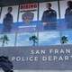 A pedestrian walks in front of a San Francisco Police Department advertisement.